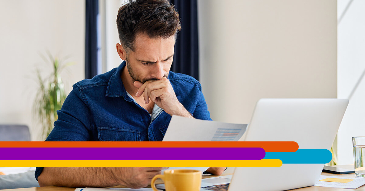 man sitting at a desk looking down at a paper bill and laptop